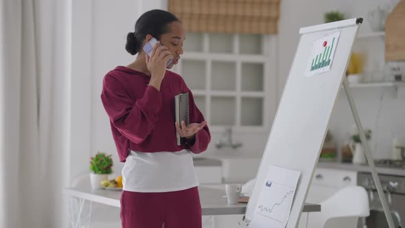 Busy Confident Young Woman in Pajamas Talking on the Phone Standing in Home Office at Whiteboard