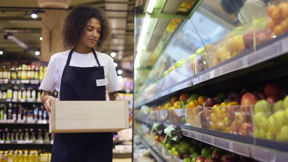 Pretty Multiracial Worker in Black Apron Stocking the Fruits in Supermarket