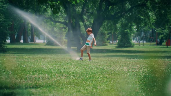 Playful Elementary Age Boy Kicking Water Sprinkler Jet