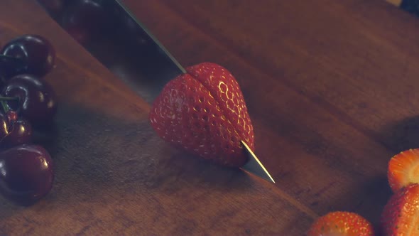 A chef knife slices through a strawberry on a kitchen counter