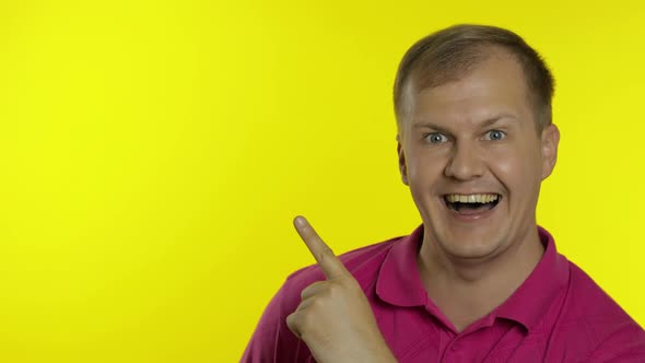 Portrait of Young Man Posing in Pink T-shirt. Happy Smiling Guy Pointing at Something with Hand