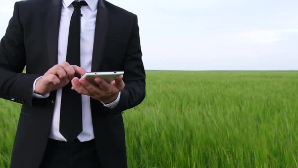 Male Businessman with Tablet in Hands on Wheat Field Background