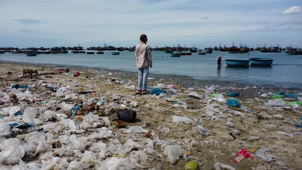 Girl Standing At The Filthy Beach With Plastic Bags And Rubbish, Looking In The Harbour With Fishing