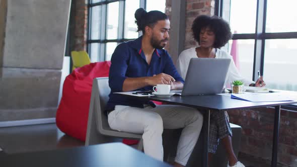 Diverse couple sitting at a table in a cafe drinking coffee using laptop and talking