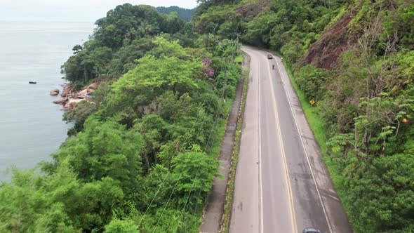 Fast Aerial flying over road along coast of Ubatuba on partly cloudy day, Brazil