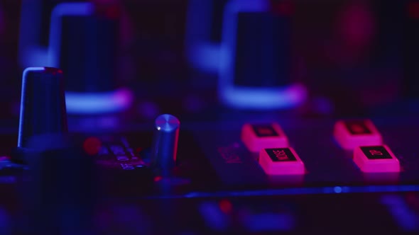 Closeup of Professional DJ Adjusting Fader on Digital Music Console in Pink Neon Light in Nightclub