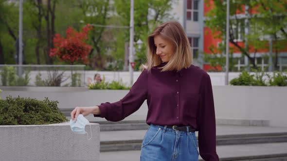 Young woman comes out of work happy and throws the mask in the trash.