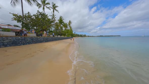 Couple walking on narrow sandy beach next to Caribbean Sea during sunny day - Fpv Drone flight