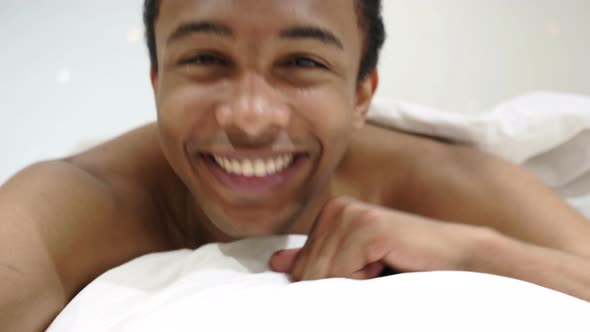 Thumbs Up by Happy African Man Lying in Bed on Stomach