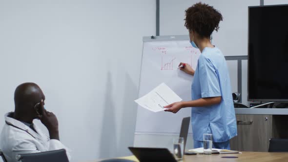 Mixed race female doctor in face mask giving presentation to african american male doctor in office