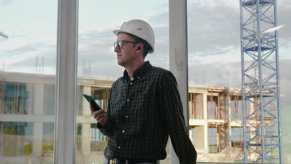 Construction Worker Listening To Music From His Phone with Wireless Headphones.