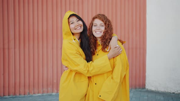 Joyful Girls Standing Outdoors Wearing Raincoats Smiling Looking at Camera