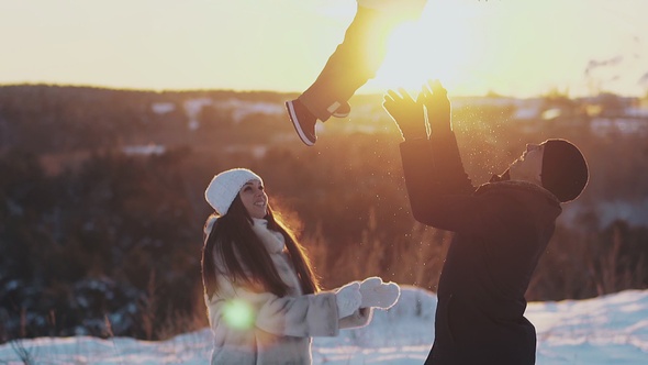 Parents play tossing child against orange sunset in winter