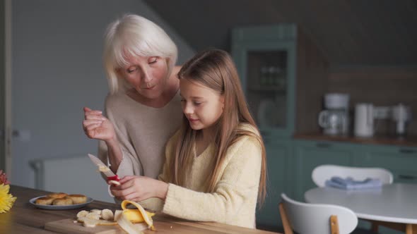 Positive girl cuts banana and eating with grandmother