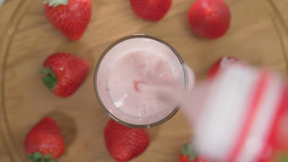 Glass Cup with Strawberry Milkshake Smoothie Fruit Juice with Milk is Poured Close Up