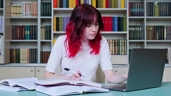 High School Student Girl Studying in School Library Using Books and Laptop alt