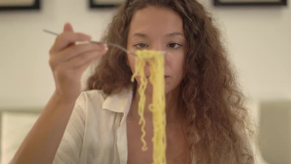 Young Woman with Loose Curly Hair Eats Fast Food Noodles