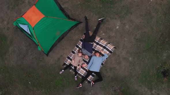 Overhead View of Young Family Lies on Blanket Near Tent and Enjoys Camp Vacation Together