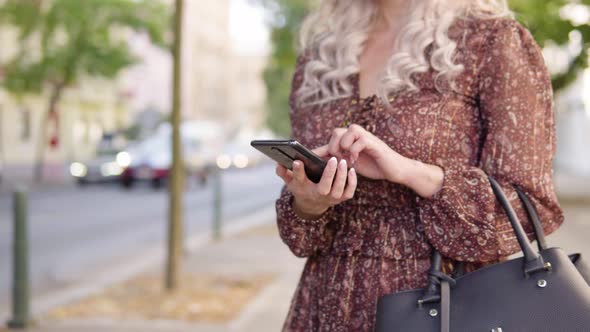 A Caucasian Woman Works on a Smartphone in an Urban Area  Closeup  a City Street