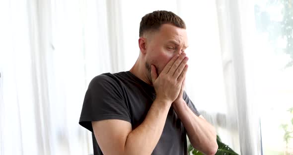 Handsome Man Sneezes Against White Curtains