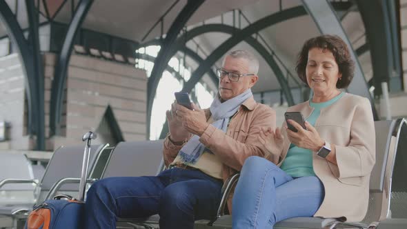 Lovely Mature Couple Using Smartphones While Waiting for Flight Sitting in Airport Terminal