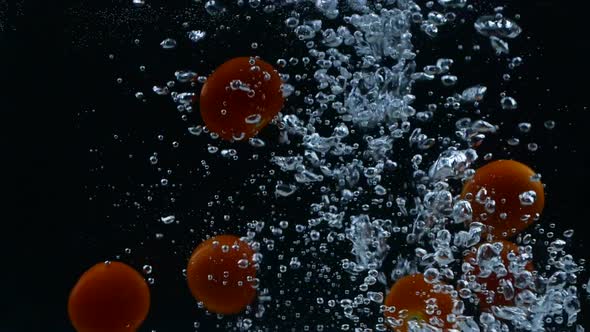 Slow motion of red cherry tomatoes falling down into water with bubbles on black background