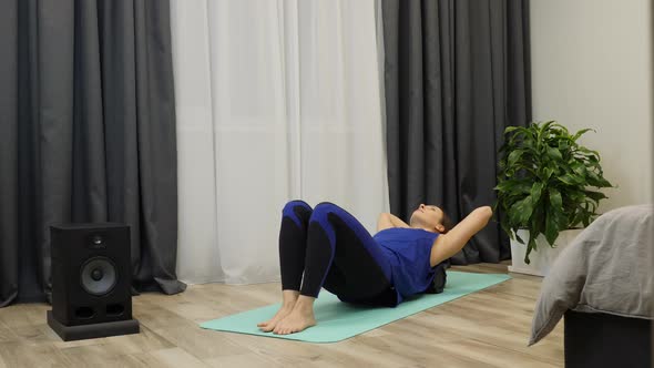 Woman massages spine muscles using roller for yoga at home in blue sportswear