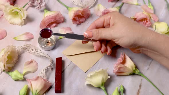 Hands pouring melted wax and sealing an envelope near pink flowers