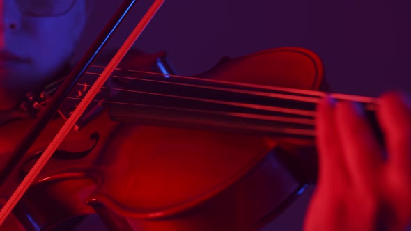 Woman Musician Plays on Strings of the Violin with Bow a Closeup in the Red Light of Studio