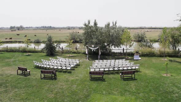 Aerial View of Empty Traditional Wedding Ceremony Set-Up with Water and Field in the Background 4K 6