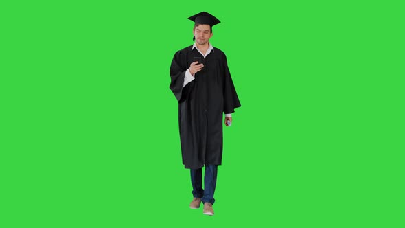 Male Student in Graduation Gown Checking His Phone While Walking on a Green Screen Chroma Key