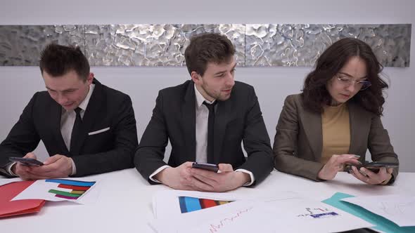 Three Concentrated Employees Sitting at Table Texting on Smartphones Talking in Slow Motion