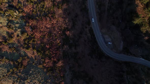 Aerial overhead shot of winding road between rocky cliffs. Rocky mountains surrounding a curved high