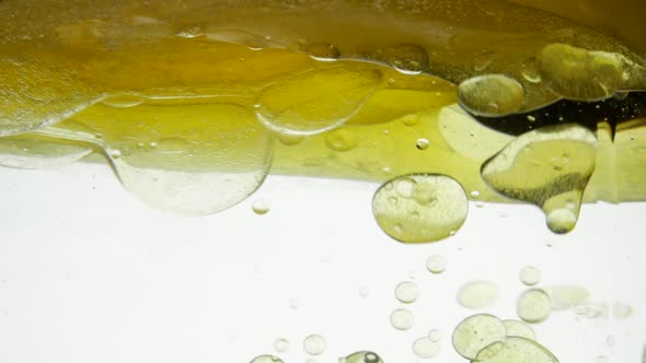 Mixing Linseed and Sesame Oil on a White Background. Pouring Golden Liquid with Water Into a Glass