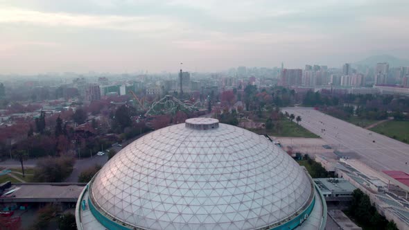 Aerial dolly in of ellipse dome music venue in O'Higgins Park revealing amusement park and city in b