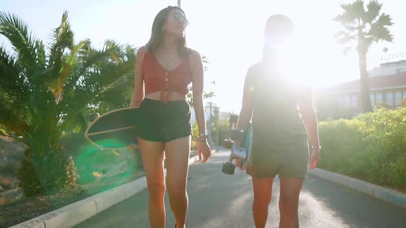 Girlfriend Girls Go To the Park Near Palm Trees Carry Skateboards in Their Hands and Talking and