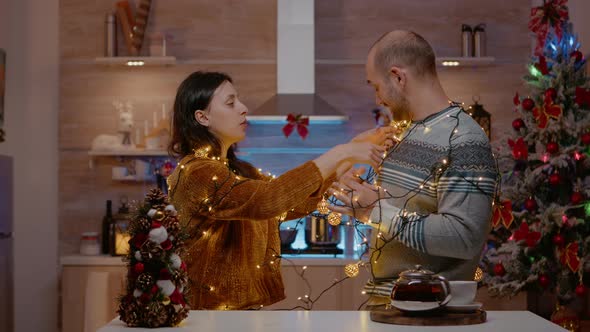 Cheerful Couple Getting Tangled in Garland of Christmas Lights