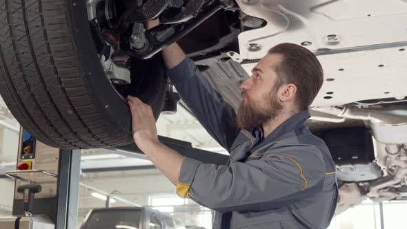 Bearded Male Mechanic Checking Wheels of a Car on a Lift at the Garage