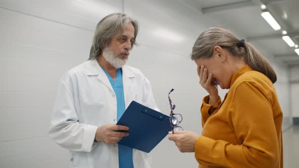 Senior Doctor in Uniform Telling Bad News To Aged Woman in Hospital Corridor