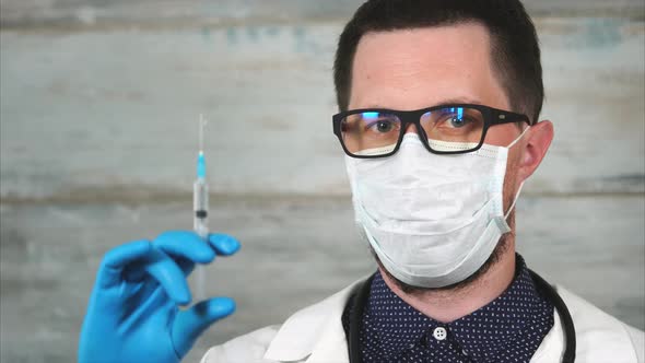 Male Scientist or Medic in White Coat and Protective Mask Holding Syringe