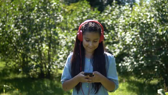 An Attractive Girl with Long Hair Walks Through the Park and Listens to Music in Headphones