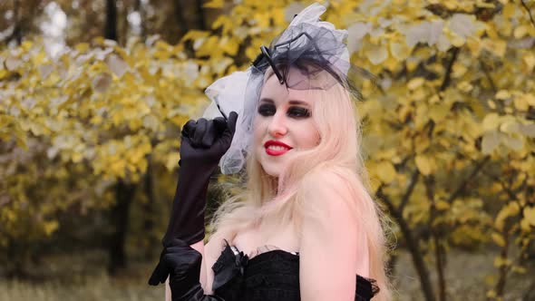 A beautiful girl in the image of a witch with black eyes and red lips. Wears black gloves and smiles