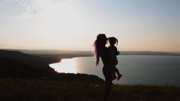 A Girl with Her Little Daughter Is Enjoying the Sunset on the Shore of Mountain Lake.