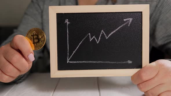 A Woman is Holding a Gold Coin Bitcoin and a Board with a Graph of Price Growth