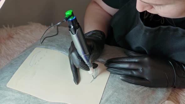 Female Hands in Black Gloves Closeup Draw an Eyebrow on a Silicone Mat with a Tattoo Machine