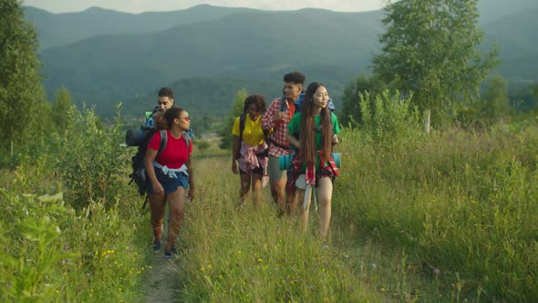 Group of Joyful Multiracial Travelers with Backpack Ascending Mountain Hill