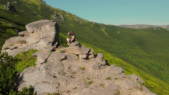 Aerial View A Young Male Athlete Sitting on the Edge of a Cliff and Looking Into the Distance