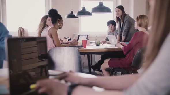 Unrecognizable Girl Typing on Laptop. Brainstorming By the Table in Modern Multiethnic Loft Office