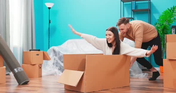 Happy Young Couple Moving Into New Apartment Boyfriend Drives Girlfriend in Cardboard Box She