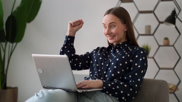 A Pretty Woman Celebrating Something While Working with a Laptop Sitting on the Couch at Home